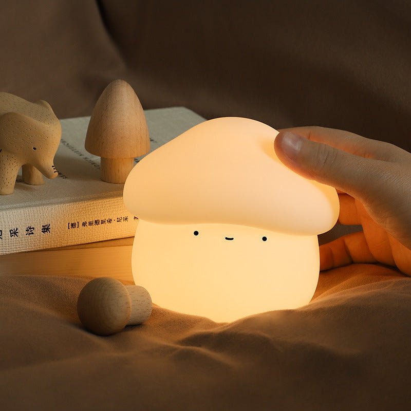 Mushroom-shaped night light being held by a hand with wooden toys and books in the background.