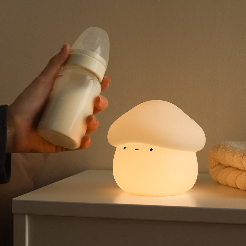 Hand holding a baby bottle next to a mushroom-shaped night light on a surface.
